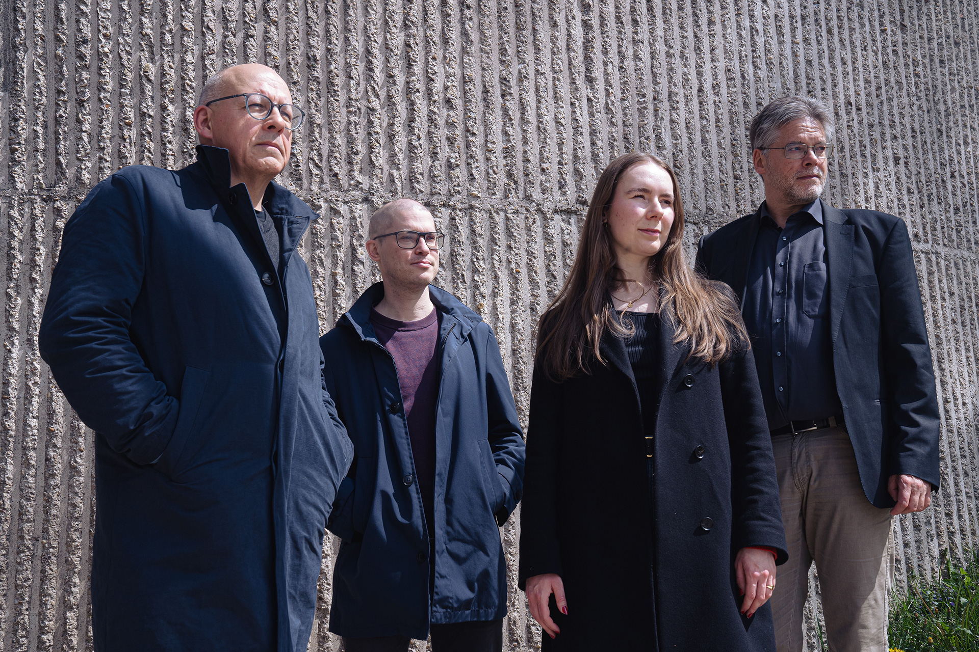 Portrait de quatre hommes et une femme devant un mur en béton