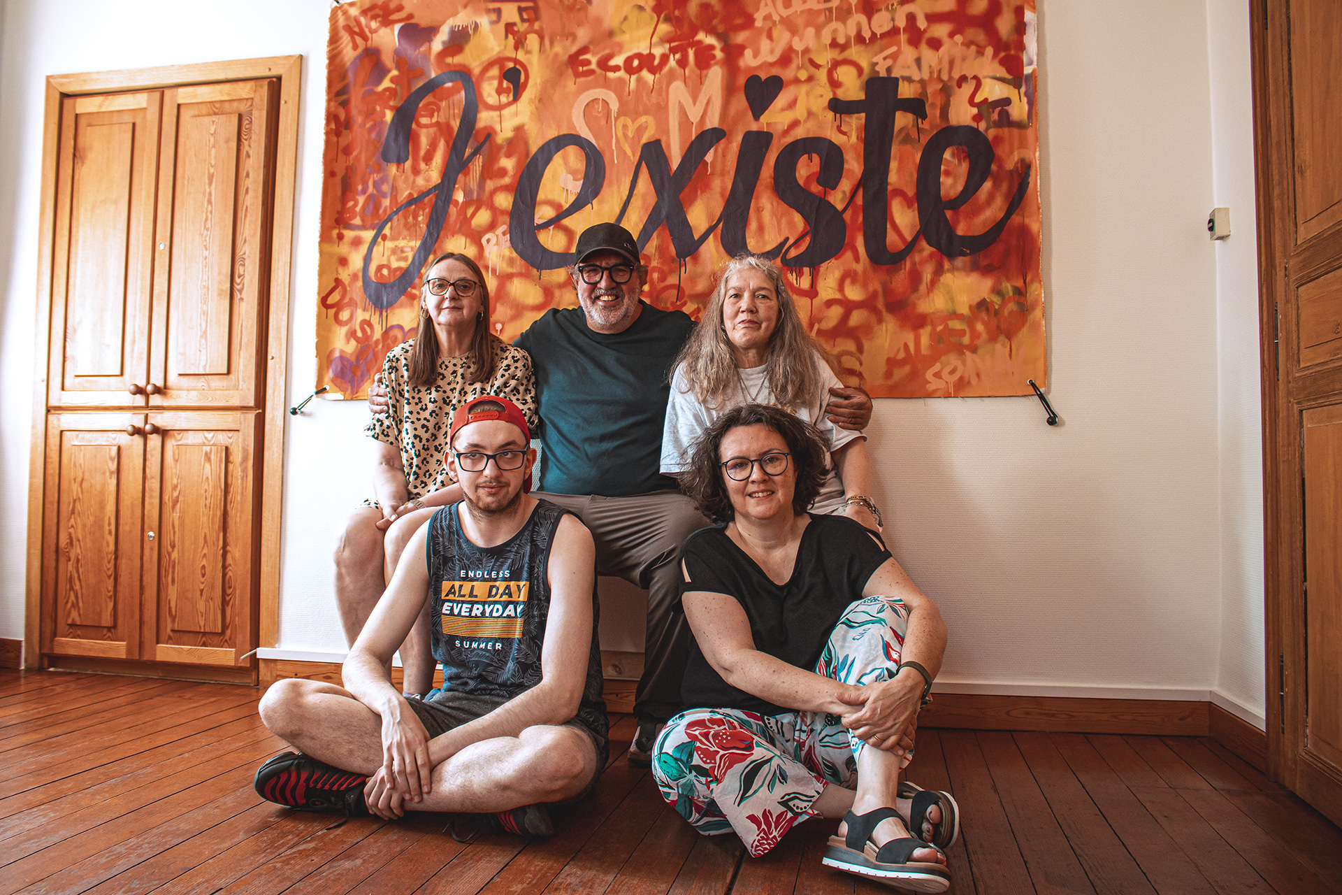 photo d'un groupe de personnes assis devant une affiche sur laquelle est écrit « J'existe »